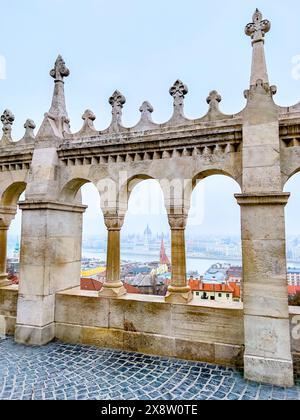 La vista attraverso le finestre della galleria del Bastione dei pescatori, che mostra il Parlamento, le case e il fiume Danubio a Budapest, Ungheria. Foto Stock