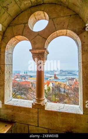 La vista attraverso le finestre della galleria del Bastione dei pescatori, che mostra il Parlamento, le case e il fiume Danubio a Budapest, Ungheria. Foto Stock