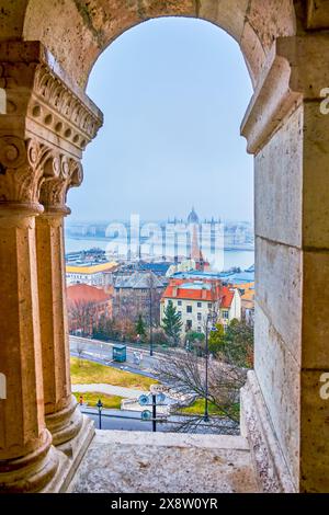 La vista attraverso le finestre della galleria del Bastione dei pescatori, che mostra il Parlamento, le case e il fiume Danubio a Budapest, Ungheria. Foto Stock