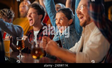 Un gruppo di amici diversi che bramano la loro squadra, bevendo birra al bancone di un pub. Tifosi di supporto tifo, applauso e urla. Amici gioiosi celebrano la vittoria dopo il gol. Foto Stock