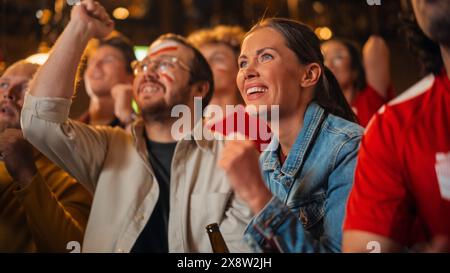 Gruppo di amici multiculturali che assistono a una partita di calcio dal vivo in un bar dello sport. Concentrati su Beautiful Female. I giovani festeggiano quando la squadra segna un gol e vince la Coppa del mondo di calcio. Foto Stock