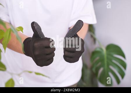 La mano che indossa un guanto di gomma mostra un cartello con il pollice, che simboleggia la sicurezza e il successo nel lavoro. Trasmette approvazione e comunicazione positiva. Soddisfazione e protezione Foto Stock