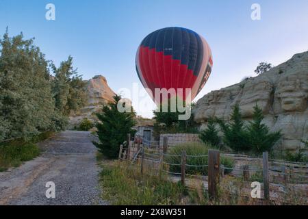 Una vibrante mongolfiera sale sul paesaggio roccioso della Cappadocia contro un cielo azzurro. Questa scena accattivante mette in mostra il brivido e la bellezza Foto Stock