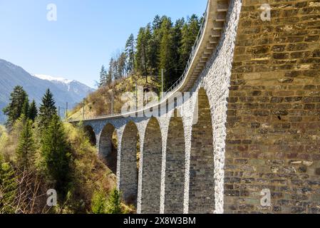 Vista ad angolo basso di un viadotto ferroviario in pietra deserto nelle Alpi svizzere in una giornata di primavera limpida Foto Stock