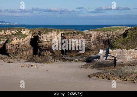 scena costiera con scogliere rocciose a strati, una spiaggia sabbiosa e un cielo azzurro Foto Stock