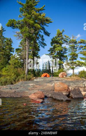 Vista verticale di una tenda arancione in un campeggio su una costa rocciosa con pini nel nord del Minnesota Foto Stock