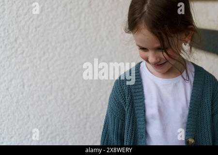 Una ragazzina sorridente imbarazzata con una maglietta e una giacca si trova vicino all'ingresso della casa Foto Stock