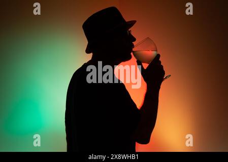 Ritratto di un uomo non identificato in silhouette che beve liquido da un vetro trasparente. Isolato su sfondo colorato. Foto Stock