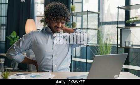 Stanco malato arabo ispanico uomo d'affari malato ragazzo soffre mal di schiena dolore alla schiena dopo computer portatile lavoro in ufficio uomo malsano business datore di lavoro Foto Stock