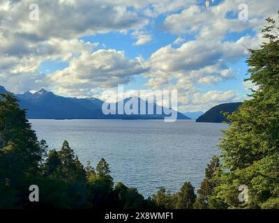 Tranquilla vista sul lago con le montagne circostanti, cielo azzurro e lussureggiante foresta verde, creando un paesaggio pittoresco e tranquillo Foto Stock