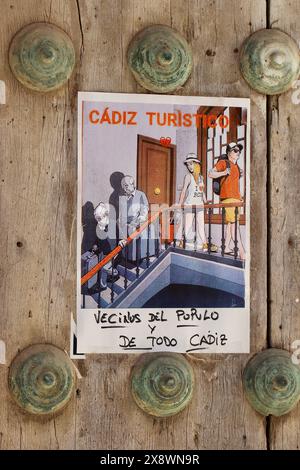Cartone animato di protesta locale su una porta di una chiesa in Spagna che mostra la gente del posto sfollata dai turisti. Recita "Neighbours of Populo (città vecchia) e tutta Cadice" Foto Stock