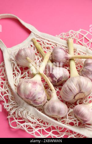 Borsa a cordoncino con teste d'aglio su sfondo rosa brillante, primo piano Foto Stock