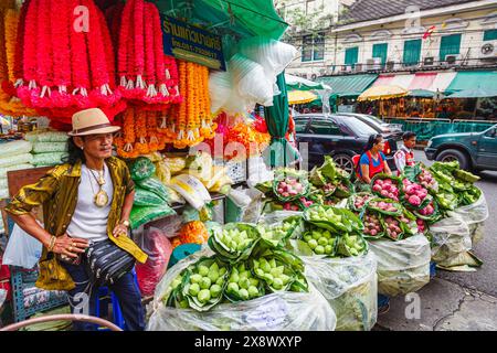 Bancarelle lungo la strada e stallholder maschile che vendono fiori colorati e ghirlande fuori dal mercato all'ingrosso dei fiori della città dei fiori di Yodpiman a Bangkok, Thailandia Foto Stock