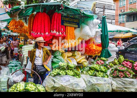 Bancarelle lungo la strada e stallholder maschile che vendono fiori colorati e ghirlande fuori dal mercato all'ingrosso dei fiori della città dei fiori di Yodpiman a Bangkok, Thailandia Foto Stock