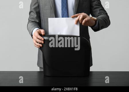 Giovane in tuta che distrugge fogli di carta in trituratore su sfondo grigio, primo piano Foto Stock