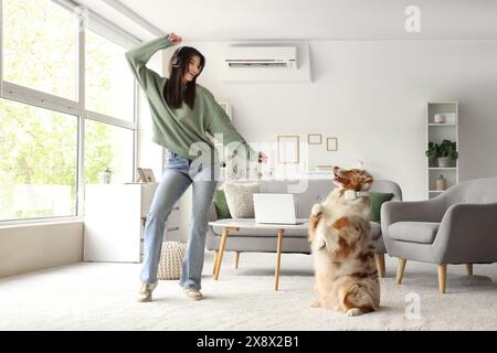 Giovane donna in cuffia con cane pastore australiano che balla a casa Foto Stock