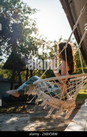 felice giovane donna cavalcata su sedia altalena macrame vicino a casa di campagna all'aperto Foto Stock