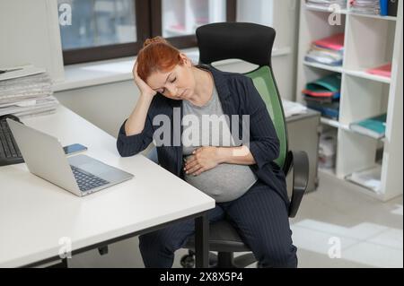 Donna incinta che dorme alla sua scrivania in ufficio. Foto Stock