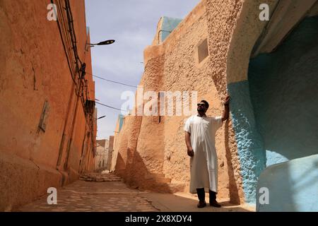 Un uomo in abito bianco in strada a Ksar beni Isguen con architetture tradizionali accanto a lui. Beni Isguen è uno dei 5 Ksar (insediamento fortificato) nella valle di Mzab. Provincia di Ghardaia. Sahara settentrionale. Algeria Foto Stock