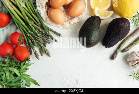 Una varietà di verdure fresche, tra cui asparagi, pomodori e rucola, sono ordinatamente organizzati accanto a avocado maturi e un sacchetto di uova scure. L'arr Foto Stock