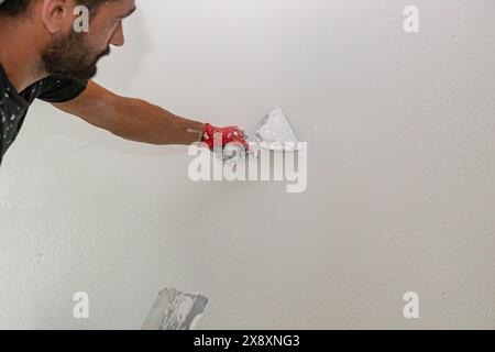 Mano con una spatola. Il lavoratore sta fissando la superficie della parete come applicazione del materiale di rivestimento della scrematura alla parete prima della verniciatura. Foto Stock