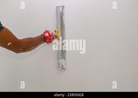 Mano con una spatola. Il lavoratore sta fissando la superficie della parete come applicazione del materiale di rivestimento della scrematura alla parete prima della verniciatura. Foto Stock