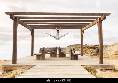 Donna che fa sport sulla spiaggia sul portico al tramonto con rocce e mare sullo sfondo Foto Stock