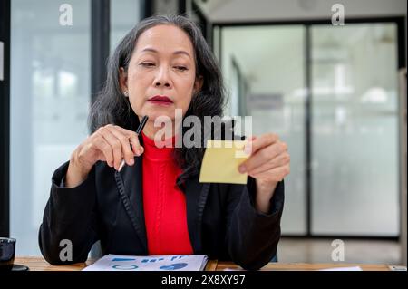 Una donna d'affari asiatica seria e premurosa che legge un appunto, pensa e pianifica il suo lavoro mentre lavora alla sua scrivania in ufficio. Foto Stock