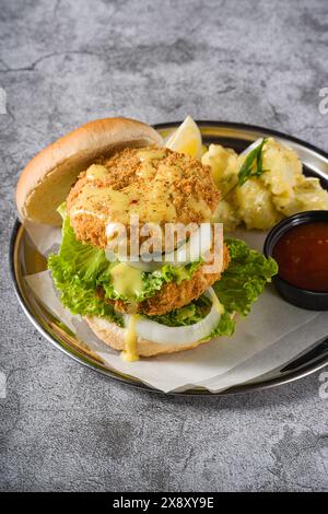 Doppio hamburger di pesce con insalata di patate su un piatto di metallo Foto Stock