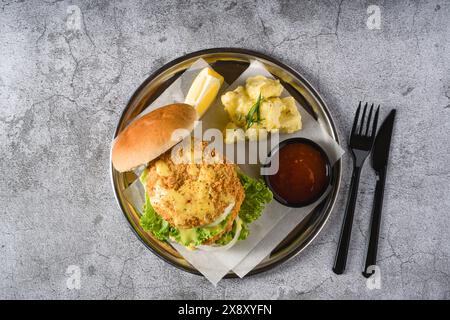 Doppio hamburger di pesce con insalata di patate su un piatto di metallo Foto Stock