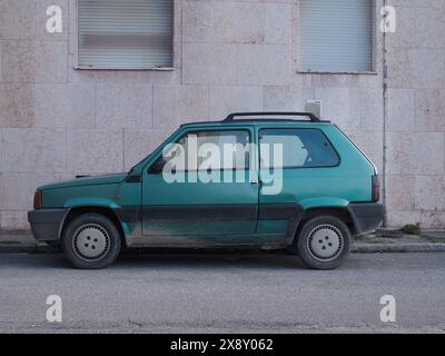 Cremona, Italia - 15 maggio 2024 Vecchia furgoncino Fiat Panda retrò di colore turchese abbandonato da un edificio con pareti intemprate, che illustra urb Foto Stock