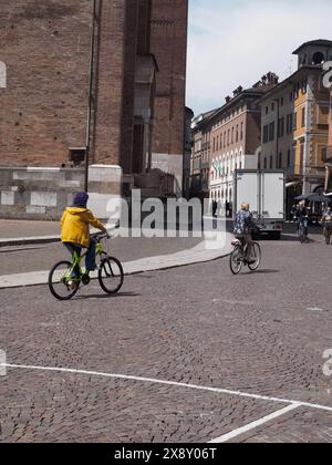 Cremona, Italia - 15 maggio 2024 i ciclisti attraversano una piazza acciottolata in italia, mettendo in mostra la vita urbana quotidiana in uno scenario di architettura storica Foto Stock