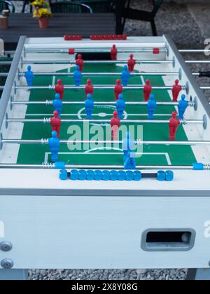 Vivace partita di calcio balilla pronta per il gioco, con figure rosse e blu allineate su un campo verde, all'aperto Foto Stock