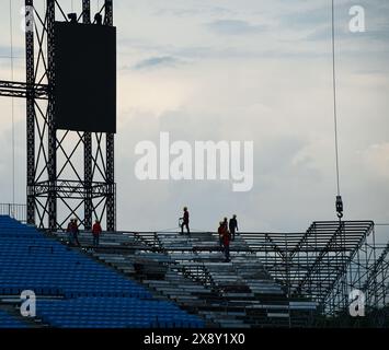 Lavoratori con cappelli e giubbotti di sicurezza che sistemano posti a sedere in tribuna, ricoperti e nuvolosi. Foto Stock