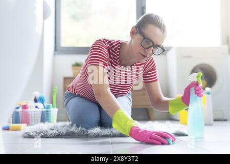 Donna che fa le faccende a casa, si inginocchia sul pavimento e pulisce le piastrelle con una spugna Foto Stock