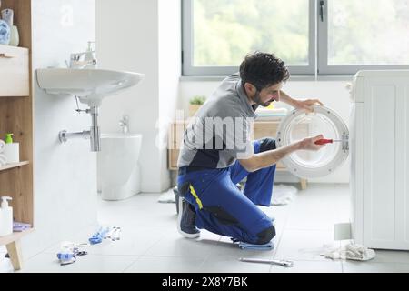 Tecnico professionista che ripara una lavatrice, sta riparando la porta Foto Stock