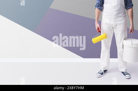Pittore professionista con rullo per pittura e secchio, è in piedi di fronte a un muro decorato con motivi geometrici e spazio di copia Foto Stock