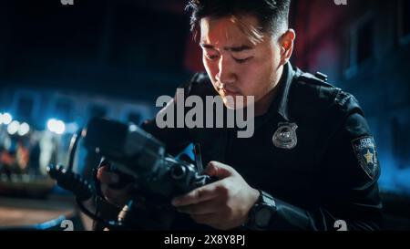 Poliziotto asiatico che scatta foto di prove su una scena del crimine di notte. L'agente di polizia scientifica trova potenziali effetti personali della vittima morta e lo fotografa per ulteriori analisi future Foto Stock