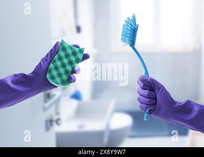 Mani femminili che indossano guanti in gomma e tengono in mano prodotti per la pulizia, bagno sullo sfondo, shot POV Foto Stock