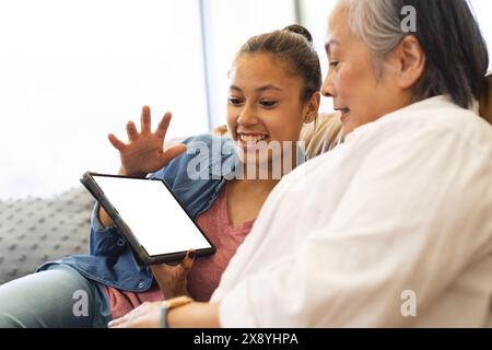 Nonna asiatica con nipotina adolescente birazziale a casa, utilizzando tablet con spazio di copia Foto Stock