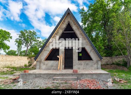 Una piccola casa con un muro di mattoni e un tetto e' in costruzione. Il tetto ha una forma triangolare. Foto Stock