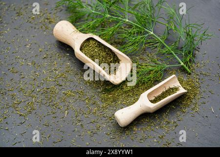 Aneto (Anethum graveolens var. hortorum), foglie di aneto essiccate e tritate con pale di legno Foto Stock