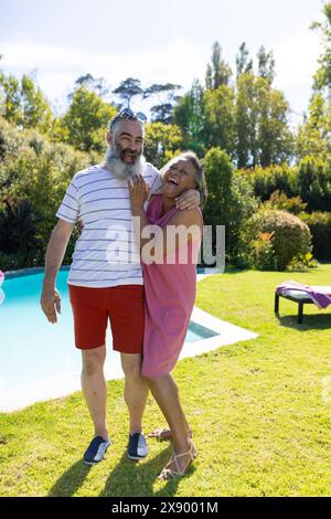 All'aperto, diversi amici anziani, ridendo vicino alla piscina, indossando abiti estivi informali Foto Stock