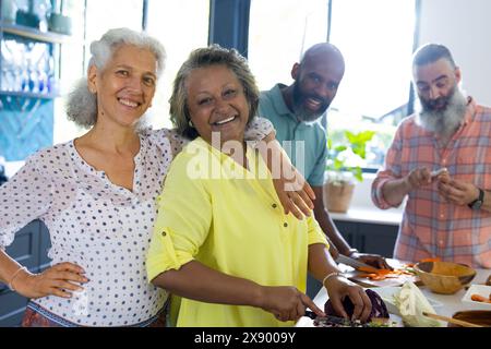 Amici anziani diversi cucinano a casa, condividendo sorrisi Foto Stock