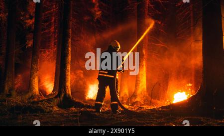 Un pompiere professionista estingue rapidamente un incendio boschivo con l'aiuto di un tubo antincendio. Fireman che salva Wildland dall'incontrollabile Brushfire con il tubo dell'acqua. Sparato da dietro. Grandangolo. Foto Stock