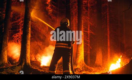 Un pompiere professionista estingue rapidamente un incendio boschivo con l'aiuto di un tubo antincendio. Fireman che salva Wildland dall'incontrollabile Brushfire con il tubo dell'acqua. Sparato da dietro. Foto Stock
