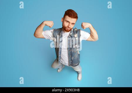 Awesome forte ragazzo caucasico mostra bicipite su sfondo blu Foto Stock