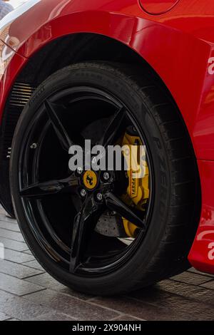Dettaglio ravvicinato di un cerchione in lega nera lucida e pinza del freno Ferrari gialla su una lussuosa auto sportiva italiana rossa. Foto Stock