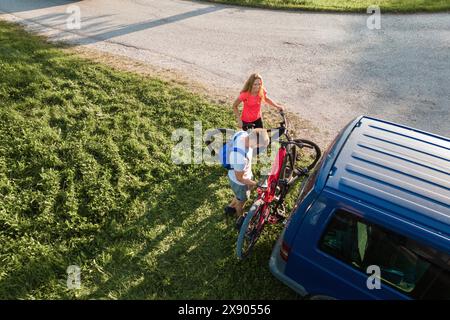 Il giovane uomo e una donna si preparano per la bicicletta fuoristrada, abbattendo mountain bike elettriche dal portabiciclette sul camper. Foto Stock
