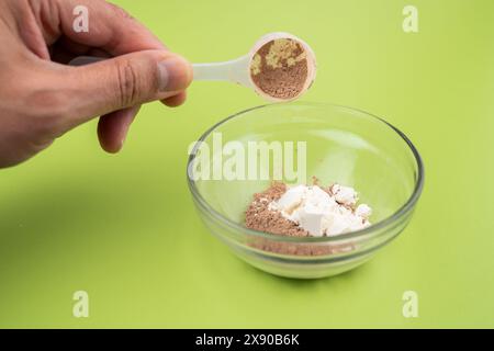 Primo piano di servire una porzione di proteina in polvere e creatina nel bicchiere dello shaker, agitare le proteine su un tavolo verde Foto Stock